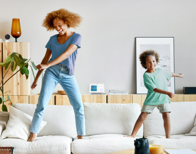 Google Nest Hub 2nd Gen on a shelf while a mother and son dance on their couch