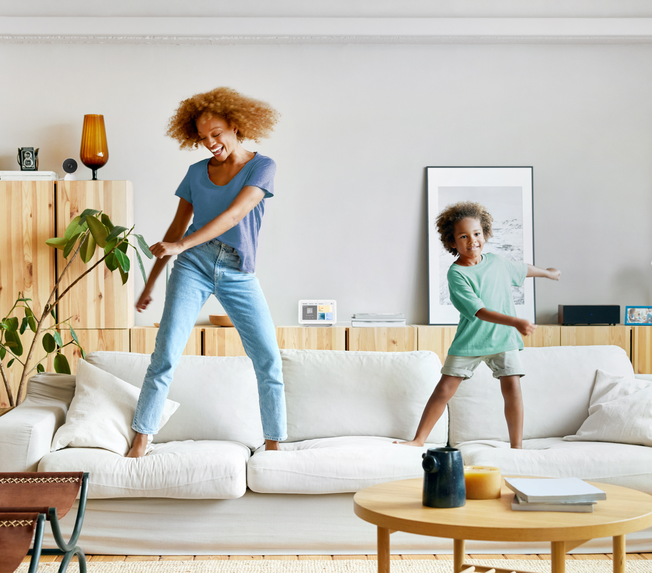 Google Nest Hub 2nd Gen on a shelf while a mother and son dance on their couch