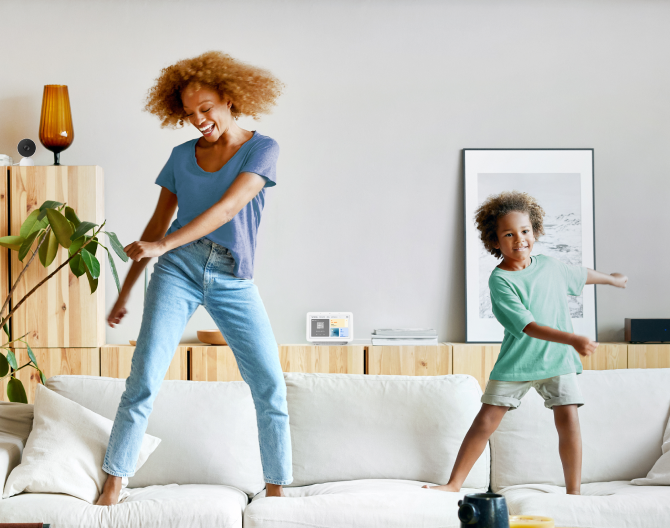 Google Nest Hub 2nd Gen on a shelf while a mother and son dance on their couch